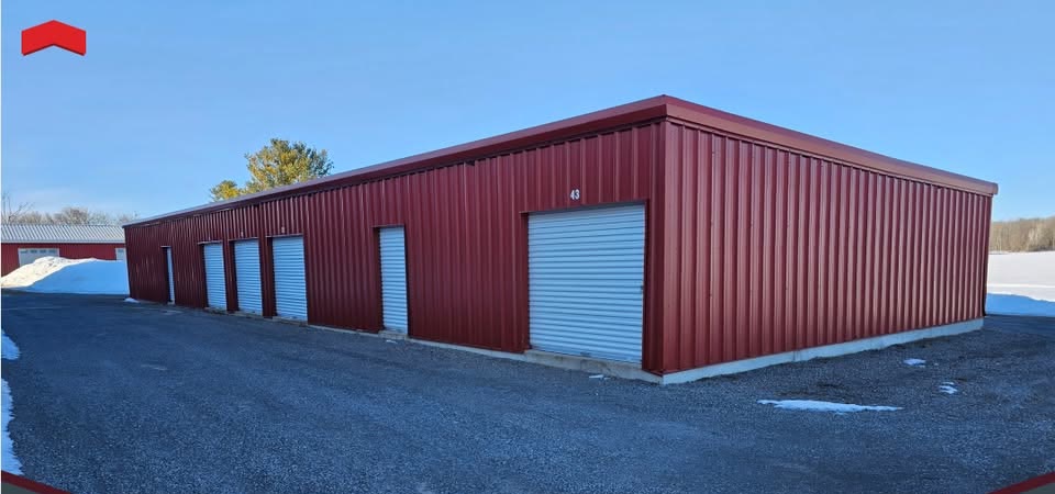 The Osgoode Storage building at 3131 River Road, a long red metal storage building with white roll-up doors and unit numbers, photographed in winter under a clear blue sky.